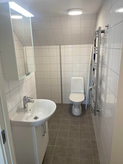 Vitt kaklat badrum med handfat och toalett.