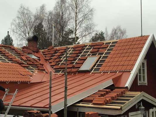 Takbyte med röda tegelpannor på ett trähus.